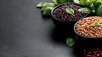 Raw legumes in black bowls with fresh basil leaves on dark background, copy space. Healthy vegan protein source, cooking ingredients for vegetarian meal.