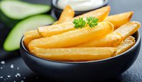 Fresh french fries in black ceramic bowl garnished with herbs and sea salt. Crispy golden potato strips served with cucumber slices on dark background.