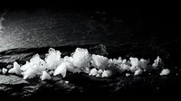 White sea salt crystals scattered on dark slate stone surface creating natural mineral texture for culinary and spa applications.