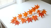 Orange maple leaf branch with vibrant autumn foliage on white surface near window, perfect for seasonal decorating and fall craft projects.