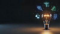 Glowing light bulb with floating digital technology icons representing innovation, creativity and business solutions on dark background.
