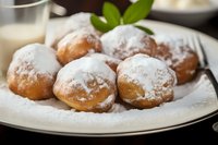 Freshly baked round donuts dusted with powdered sugar served on white plate with mint garnish and glass of milk in background.