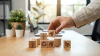 Hand arranging wooden blocks with environmental sustainability icons on office desk. Corporate responsibility and green business concept for presentations.