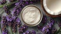 Organic coconut cream in glass jar surrounded by fresh lavender flowers on stone background for natural skincare products.