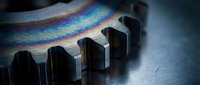 Close-up of metallic gear teeth with rainbow light refraction creating prismatic colors across industrial machinery surface for engineering concepts.