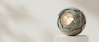 Metallic spherical sculpture with glowing orb center on white pedestal, modern art installation for contemporary interior design and gallery displays.