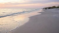Serene beach at sunset with gentle waves washing onto pristine sand shore under pastel sky creating peaceful coastal atmosphere for relaxation and meditation.