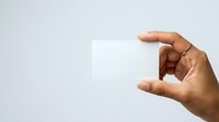 Hand holding blank white card or paper against neutral background, suitable for business presentations, advertising mockups, and promotional materials.