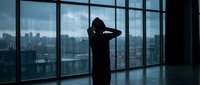 Silhouette of businessman standing by office window overlooking city skyline, contemplating future business decisions and urban development opportunities.