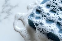 Blue soap bar with rich white foam bubbles on marble surface for bathroom hygiene and skincare routine cleaning products.