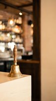 Brass service bell on counter in upscale restaurant with warm lighting and blurred dining room background for hospitality and customer service concepts.
