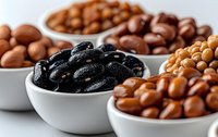 Assorted nuts and dried fruits in white ceramic bowls on white background. Close up view of healthy snacks including black raisins and mixed nuts.