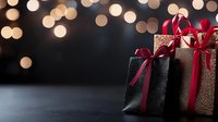 Elegant gift boxes wrapped in glittering black and gold paper with red satin ribbons against dark background with soft bokeh lights creating festive holiday atmosphere.