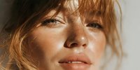 Young blonde woman with freckles and natural makeup in warm sunlight creating beautiful shadows on face for skincare and beauty concepts.
