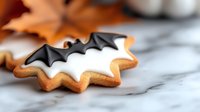 Homemade Halloween sugar cookie decorated with white royal icing and black bat design on marble surface, festive autumn holiday baking treat.