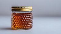 Golden honey in decorative glass jar with honeycomb pattern texture and metal lid on neutral background, showcasing natural organic sweetener.
