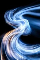 Swirling blue and white light streams with warm golden accents flow dynamically against a dark background, creating an abstract energy effect suitable for modern design, technology, and creative projects.