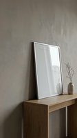 Minimalist interior mockup with blank silver frame leaning on textured wall above wooden console table with decorative vase and dry branches.