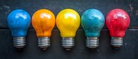 Colorful painted light bulbs arranged in row on dark background - blue, orange, yellow, turquoise and red bulbs showcase creative thinking and innovation concept.