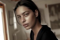 Young mixed race woman with natural makeup and black hoodie looking at camera with confident expression in soft window light, beauty portrait.