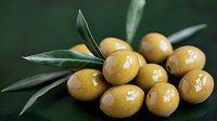 Fresh green olives with leaves on dark background, macro shot showing detailed texture and natural shine of Mediterranean fruit for food photography.