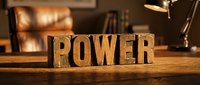 Wooden block letters spelling POWER on a rustic desk with warm bokeh background, evoking strength, leadership, and motivation in a cozy office setting.