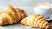 Fresh baked flaky butter croissants served with hot cappuccino in white cup on light gray background, morning breakfast composition.