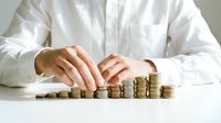 Young adult male with light skin tone wearing white business shirt arranging stacked coins in ascending order on white surface, representing financial growth, savings, investment strategy and wealth accumulation for business concepts.
