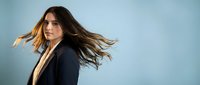 Young professional woman with flowing brown hair in motion against blue background, business portrait for corporate branding and marketing materials.