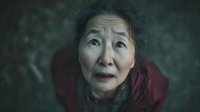 Elderly Asian woman with worried expression wearing burgundy coat against dark textured background for dramatic portrait photography and storytelling concepts.