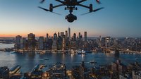 Professional drone capturing stunning aerial view of illuminated Manhattan skyline at golden hour with harbor waters and urban architecture below.