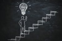 Chalk drawing on blackboard showing person climbing stairs towards lightbulb, representing growth mindset and path to innovation. Success concept for business.