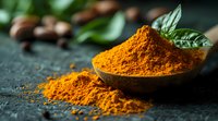 Ground turmeric powder in rustic bowl with fresh basil leaves and scattered spice on dark textured surface, warm golden spice illuminated by natural light.