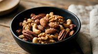 Mixed nuts assortment in black bowl with walnuts, pecans, cashews and almonds on rustic wooden table for healthy snacking and cooking ingredients.