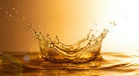 Golden liquid splash creating crown-shaped formation with droplets against warm amber background for beverage and luxury product advertising.