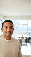 Portrait of a smiling African American man wearing a beige sweater in a bright modern office or home interior with large windows and contemporary furnishings.
