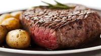 Juicy grilled beef steak cooked medium rare served with roasted baby potatoes and fresh rosemary on white plate, close up view of meat texture.