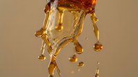 Liquid amber or honey dripping and splashing against neutral background, suitable for cosmetics, skincare, wellness and food product marketing.