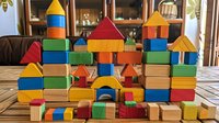 Colorful wooden building blocks arranged as castle or city structures on wooden table, featuring geometric shapes in primary colors for educational play and development.