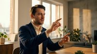 Professional Caucasian businessman in navy suit gesturing during presentation or meeting in modern office with natural lighting and plants.
