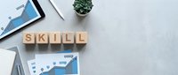 Wooden blocks spelling SKILL on a concrete desk with charts, tablet, and plant, representing professional development and career growth.