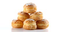 Fresh cream puffs with powdered sugar dusting arranged in pyramid shape on white background, golden brown pastry shells filled with custard cream.