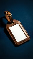 Brown leather luggage tag with blank white label and brass buckle on dark blue background for travel identification and personalization.