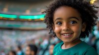 Young African American girl with curly natural hair and bright smile wearing green shirt at sports event, stadium crowd in blurred background. Candid joyful expression.