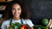 Happy young African American female chef holding fresh broccoli and tomato in professional kitchen, promoting healthy cooking and organic vegetables for culinary content.