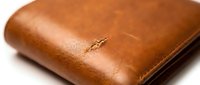 Worn tan leather wallet with visible creasing and patina marks, showing age and regular use for business or personal finance storage.