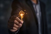 Businessman holding glowing golden key with magical sparkles against dark background, symbolizing success and unlocking business potential.