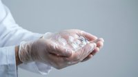 Healthcare professional wearing gloves holds transparent gel sanitizer in cupped hands for hygiene and infection prevention in medical setting.