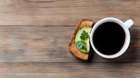 Fresh black coffee in white ceramic cup with avocado toast garnished with parsley on rustic wooden background, top view composition for food blogs and cafes.