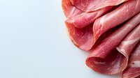 Fresh sliced prosciutto arranged in delicate folds against white background, showing marbled texture and rich pink color. Premium cured meat for culinary use.